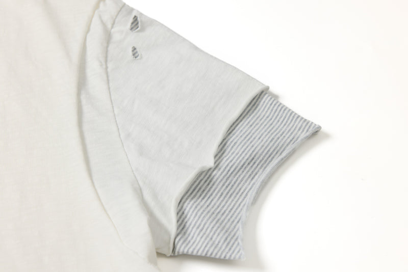 Close-up of a white distressed layered tee with frayed cutout details and striped inner sleeve on a clean background