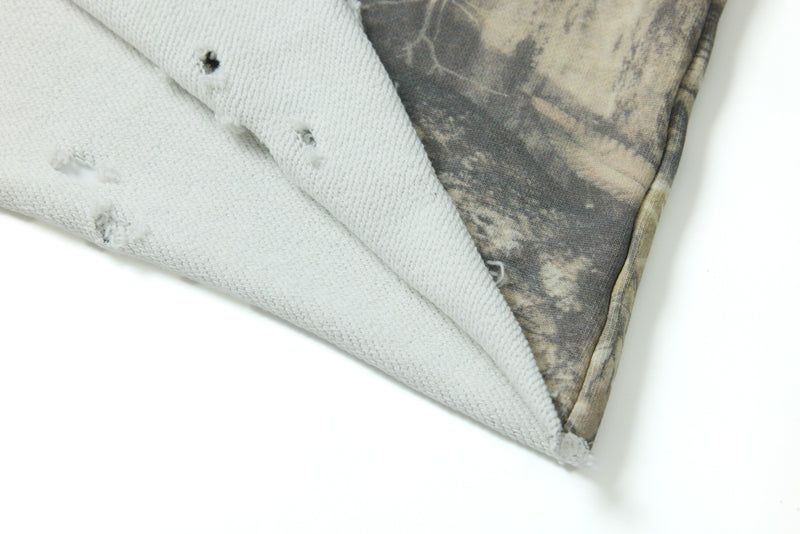 Folded white crop tee with distressed holes and faded woodland camouflage print on the sleeve and side seam