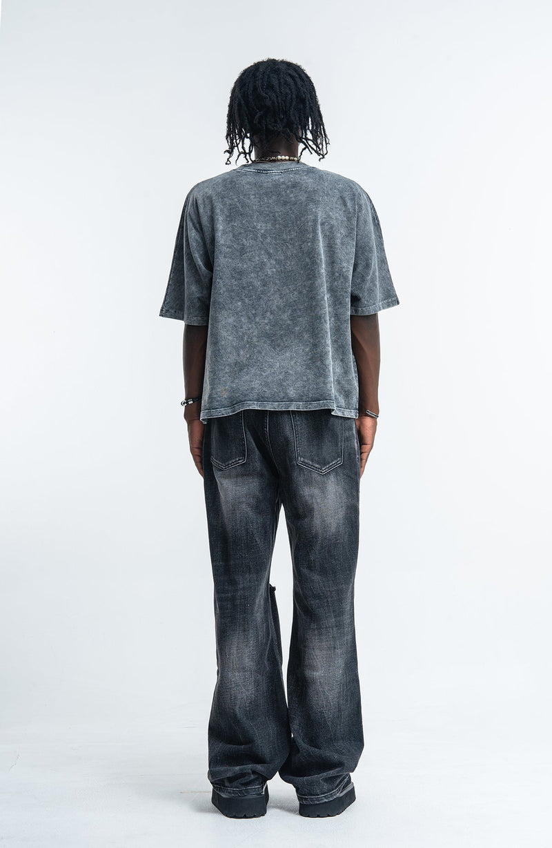 Vintage wash oversized black graphic tee with a faded acid-wash finish and relaxed fit, shown from the back with wide-leg jeans