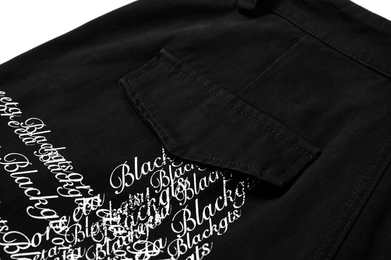 Close-up of cargo pocket and white cross script print on black pants