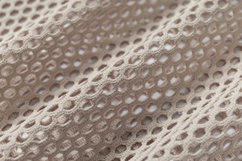 Close-up of beige mesh football jersey fabric with open weave and textured retro streetwear look