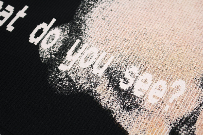 Close-up of a black streetwear T-shirt with distressed glitch text and a beige halftone graphic print