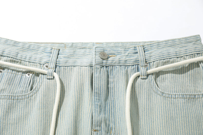 Close-up of the front waistband, button closure, and drawstring on striped denim pants