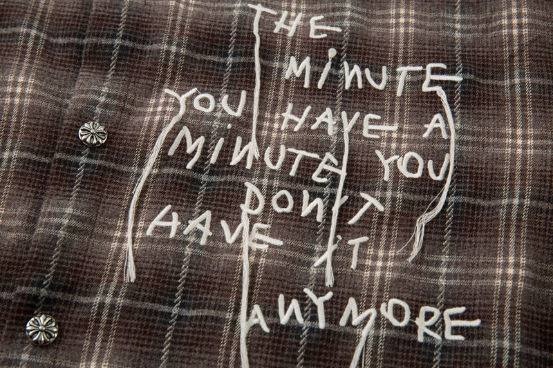Close-up of white handwritten-style graphic text on brown plaid shirt front