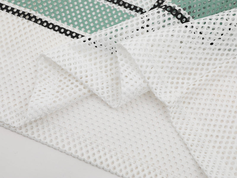 White mesh jersey fabric with perforated texture and black trim, shown in a close-up streetwear apparel detail shot