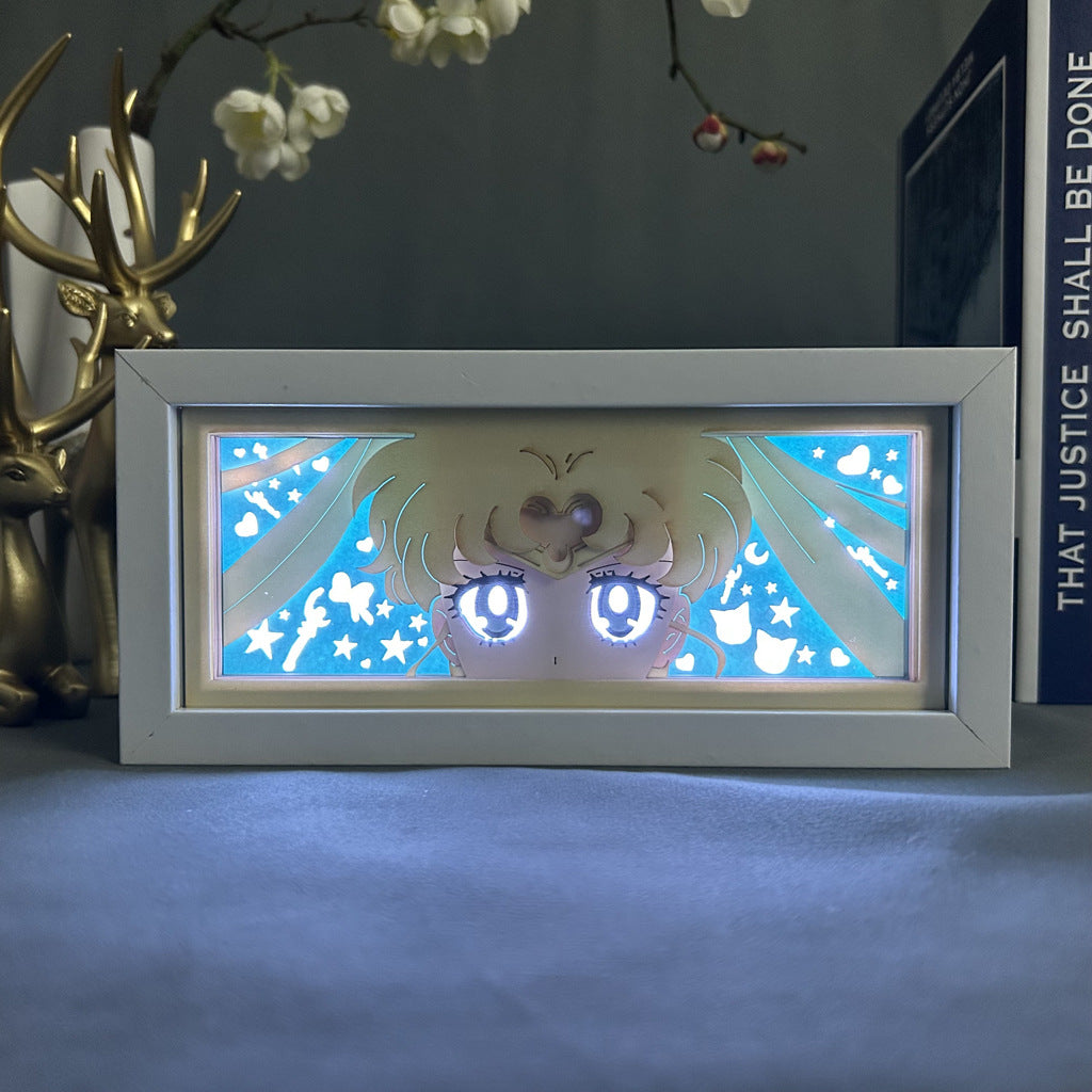 The Sailor Moon LED Light Box – Magical Girl 3D Anime Night Lamp features a framed anime character with large eyes, styled like Sailor Moon. Stars and shapes enhance the background, while a decorative deer figure and book sit nearby on a floral-accented surface.