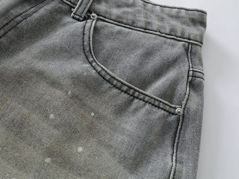 Close-up of front pocket seam on grey wash denim shorts with speckled fade and rivet detail