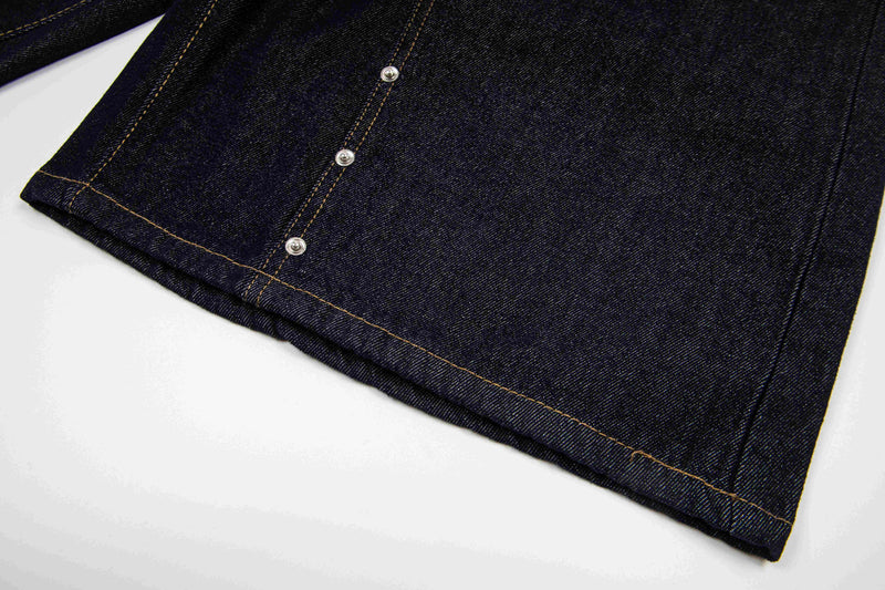 Close-up of hem and side seam on dark wash denim shorts with snap accents