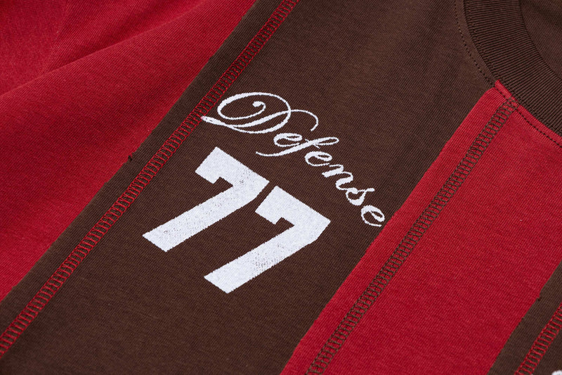 Close-up of a retro striped sports tee with brown and red panels, white oversized number 77, and vintage defense lettering