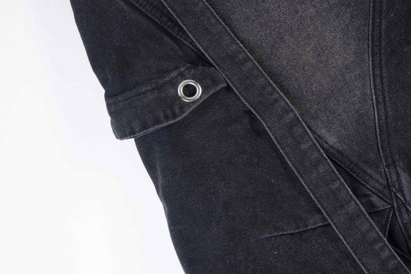 Close-up of black denim side cargo pocket with metal grommet and strap detail