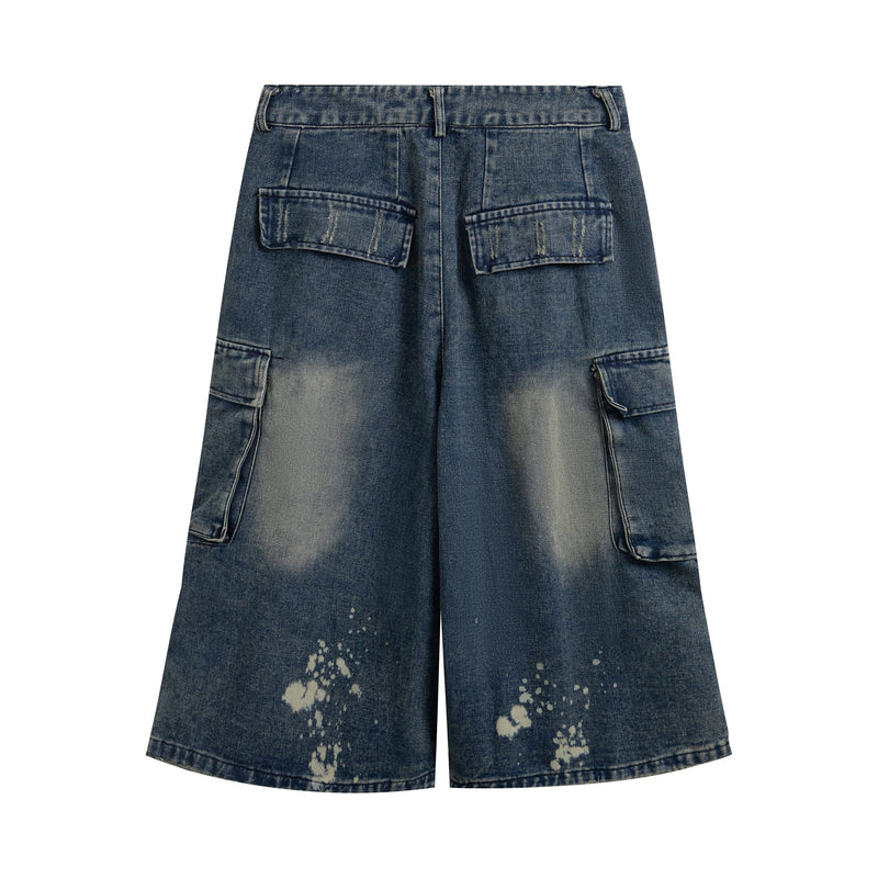 Front view of blue distressed wide-leg denim cargo shorts with flap pockets and bleach splatter