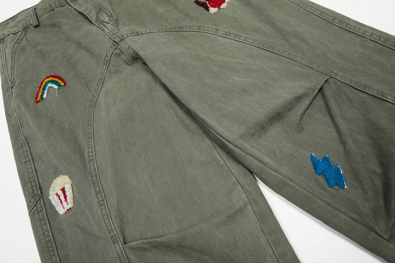 Close-up of olive green pants with rainbow, popcorn and blue lightning embroidery
