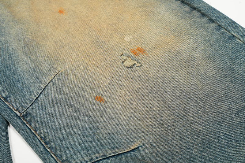 Close-up of denim fabric with small ripped hole and orange paint-like marks