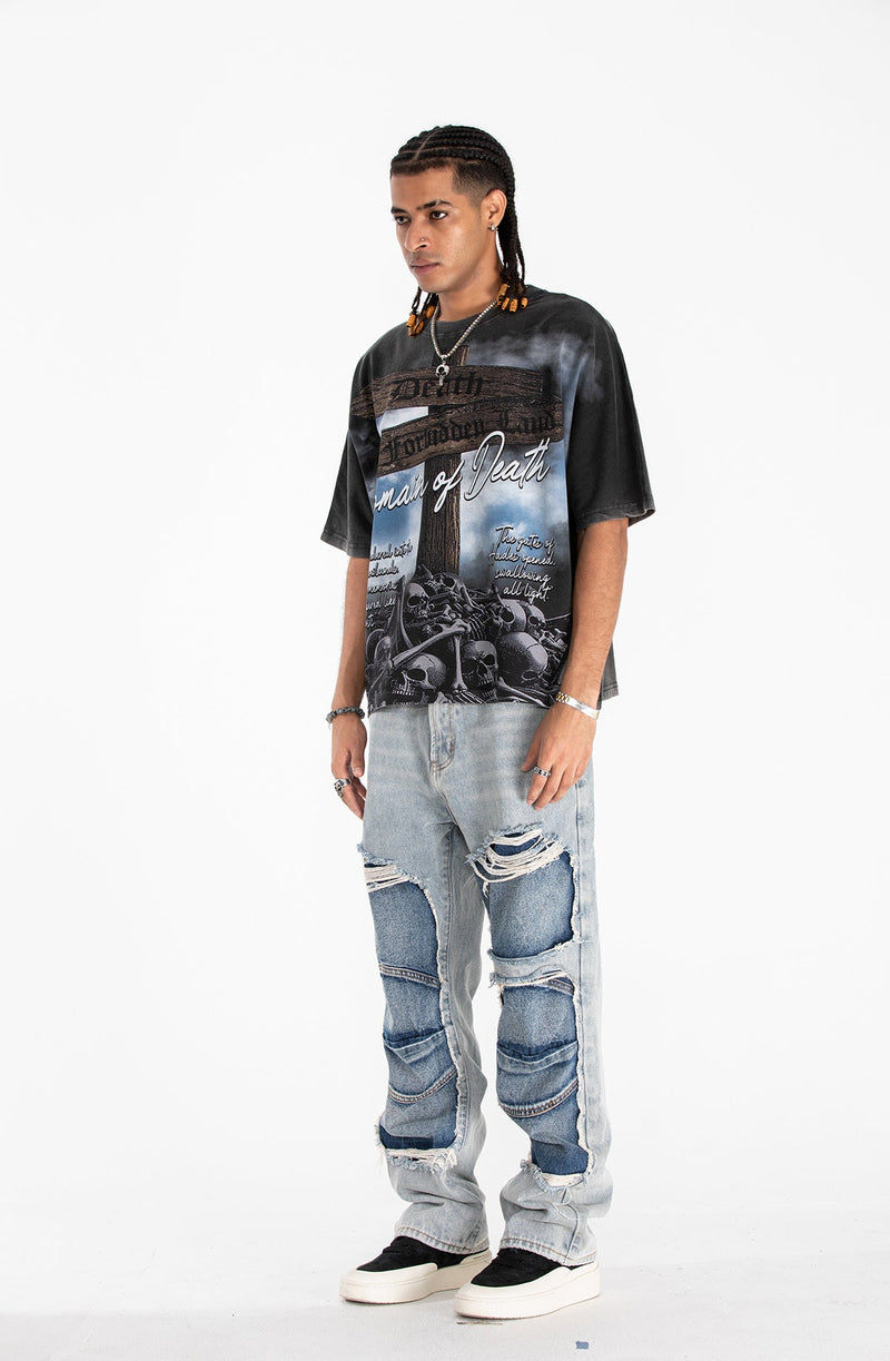 Black gothic graphic tee with skull print and worn streetwear styling worn with distressed patchwork jeans
