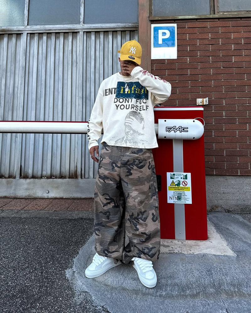 Model wearing cream graphic long sleeve shirt with camo pants and white sneakers