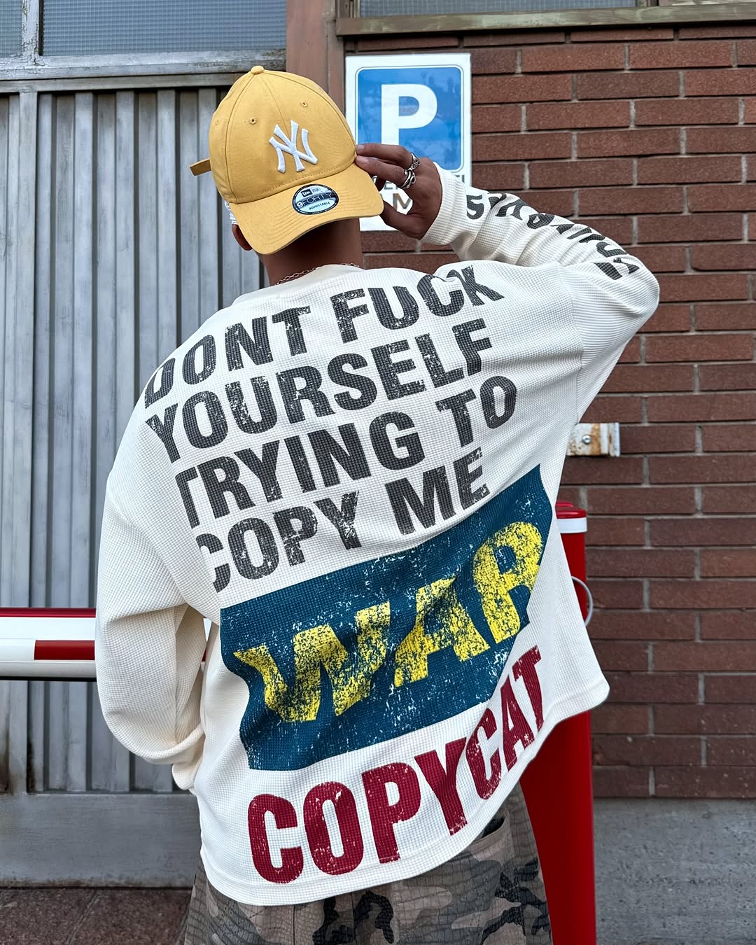 Person wearing cream oversized waffle long sleeve with COPYCAT WAR distressed back graphic and NY Yankees cap