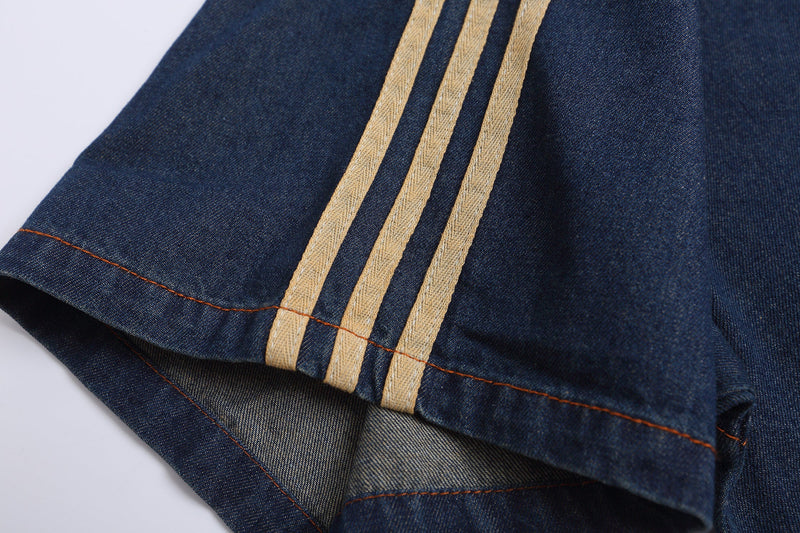 Close-up of a dark denim streetwear tee with beige triple stripes and contrast orange stitching