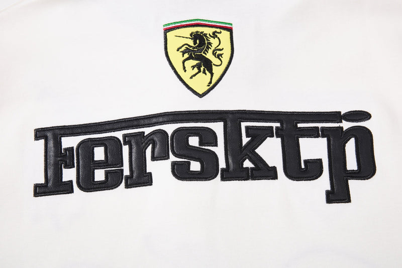 White polo shirt with Ferrari-style crest and bold black embroidered streetwear graphic across the chest