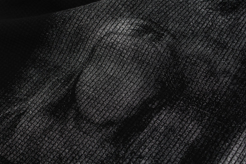 Close-up of black textured fabric on a studded mock-neck graphic tee with subtle shadow portrait detailing