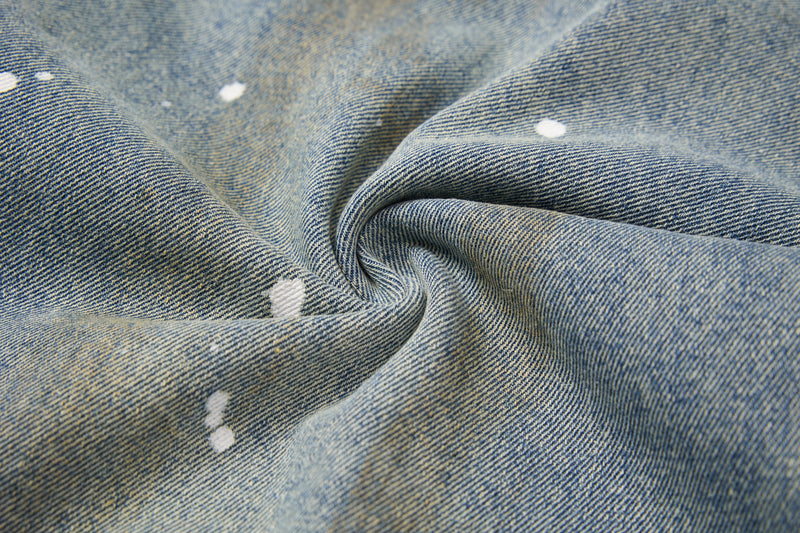 Close-up of blue denim fabric with soft folds, faded wash, and paint splatters