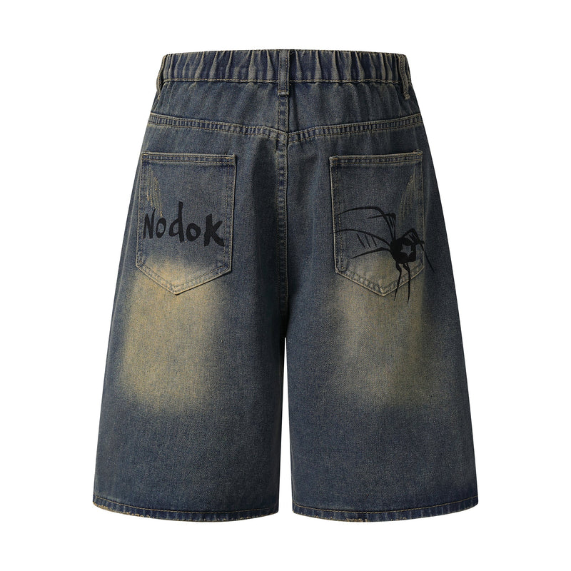 Back view of blue denim shorts with patch pockets, faded wash, and spider web graphic