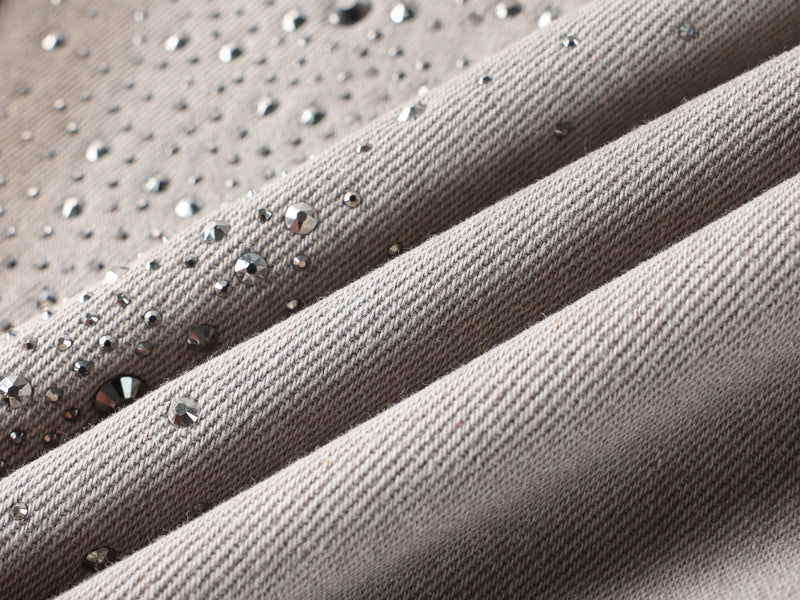 Close-up of folded denim fabric with rhinestone detail and washed gray tones
