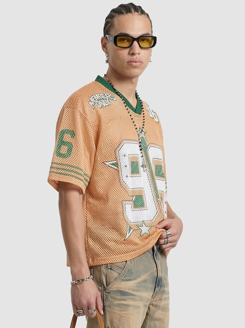Model wearing an orange mesh jersey T-shirt with green trim, large 96 graphic, and streetwear styling with sunglasses and jewelry