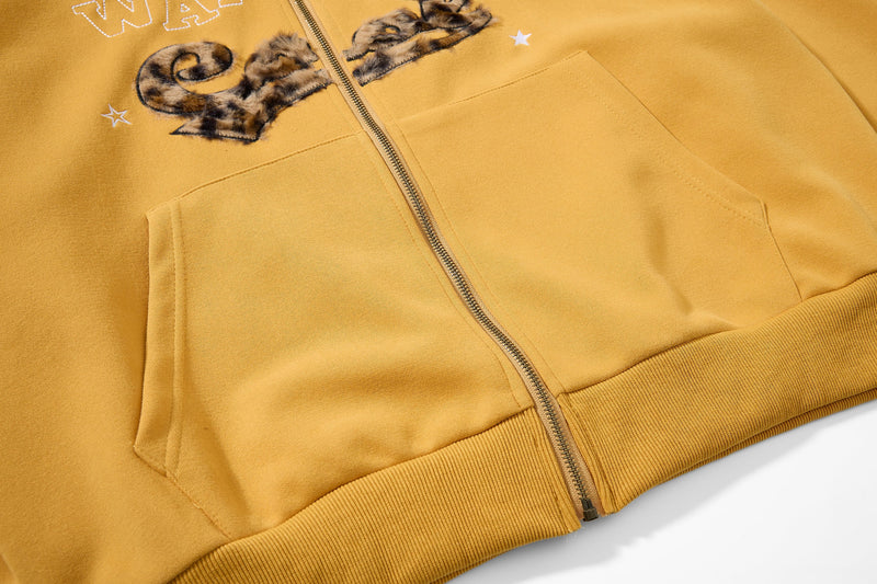 Close-up of mustard yellow hoodie front pockets, zipper, and lower hem