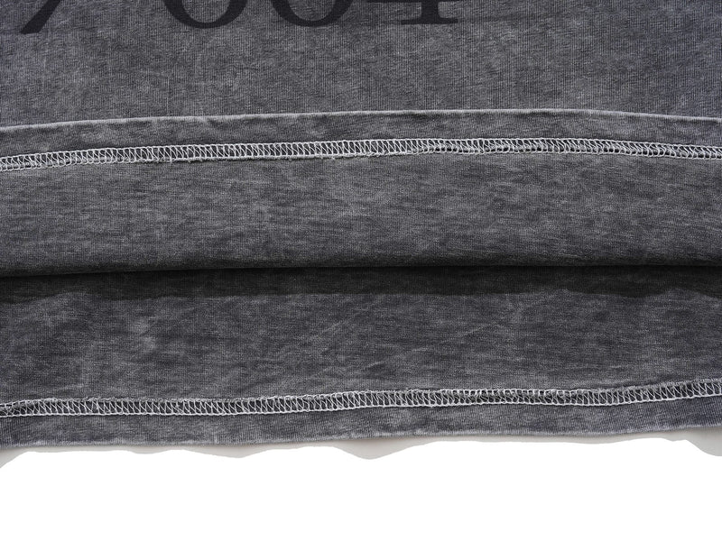 Close-up of faded black vintage wash tee fabric with visible raw hem stitching and distressed texture
