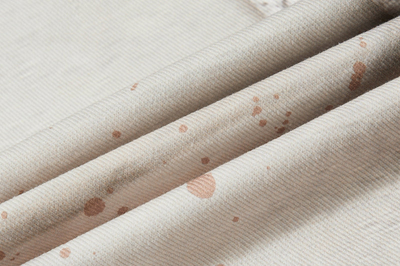 Close-up of cream denim fabric with fine ribbed texture and brown splatter print