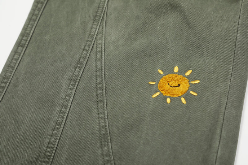 Close-up of olive green pants with smiling sun embroidery on leg