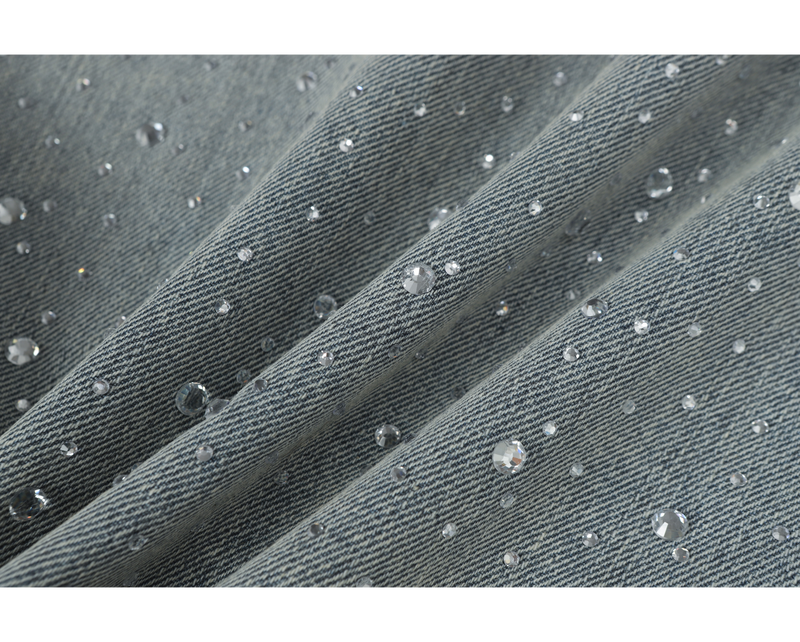 Close-up of light-wash denim fabric with diagonal folds and rhinestone details