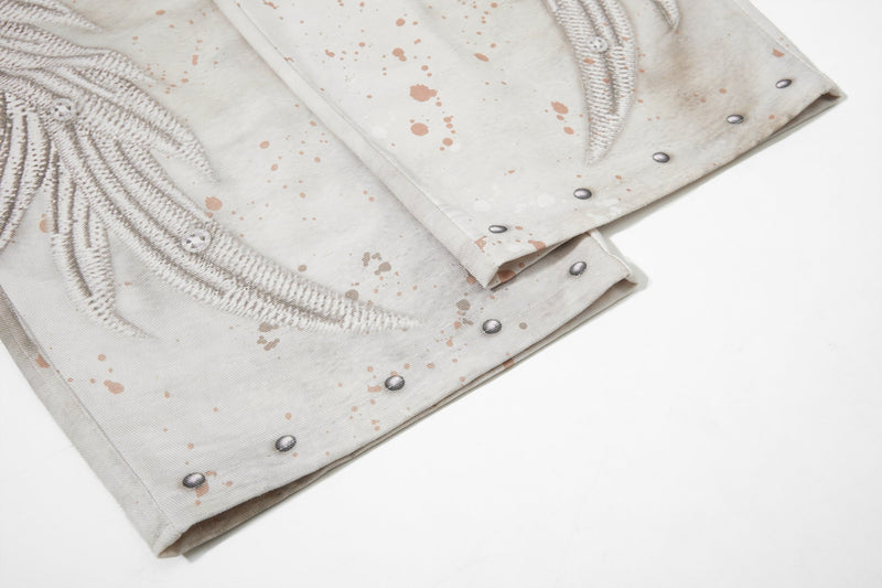 Close-up of cuffed hem on cream jeans with wing graphic and studded edge