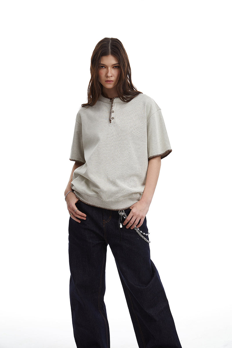 Relaxed-fit cream Henley tee with contrast stitching, short sleeves, and button placket on a model with dark jeans