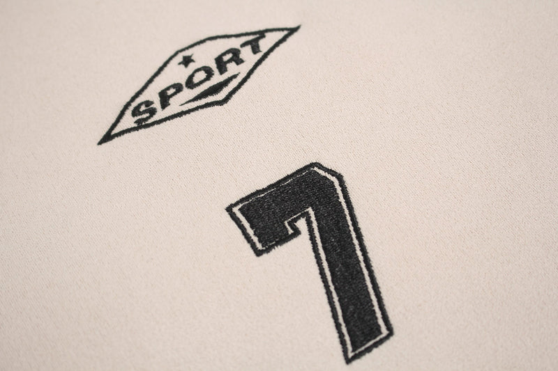 Close-up of cream athletic tee fabric with black embroidered SPORT badge and bold panel graphic accents