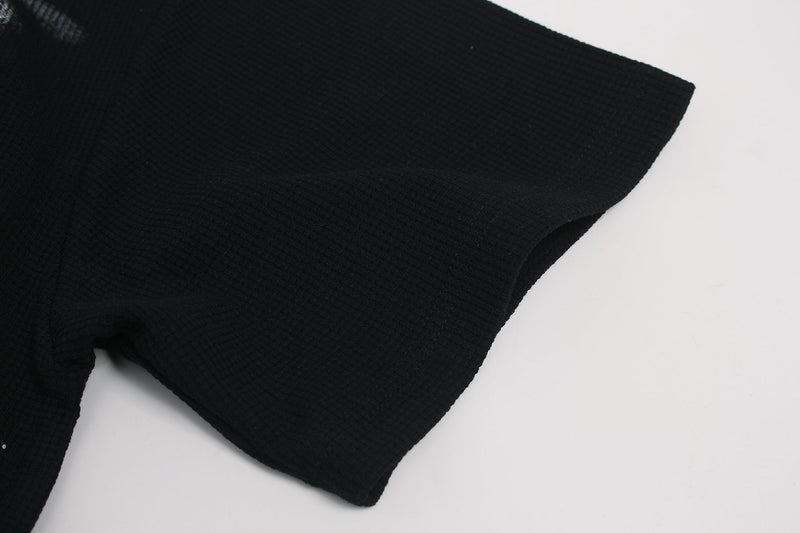 Black ribbed graphic tee sleeve on a minimalist white background, showing the bold streetwear shirt fabric texture