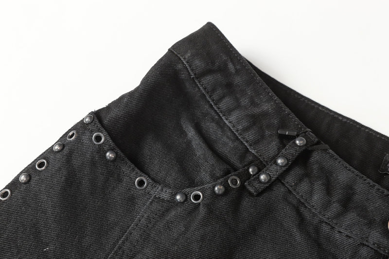Close-up of black denim waistband corner with studded trim and eyelet detail