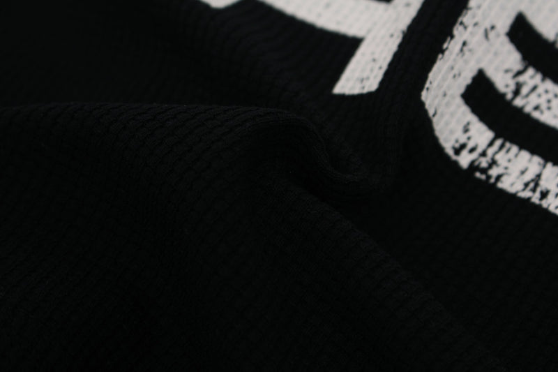 Close-up of a black streetwear tee with bold white cross typography graphic print on textured fabric