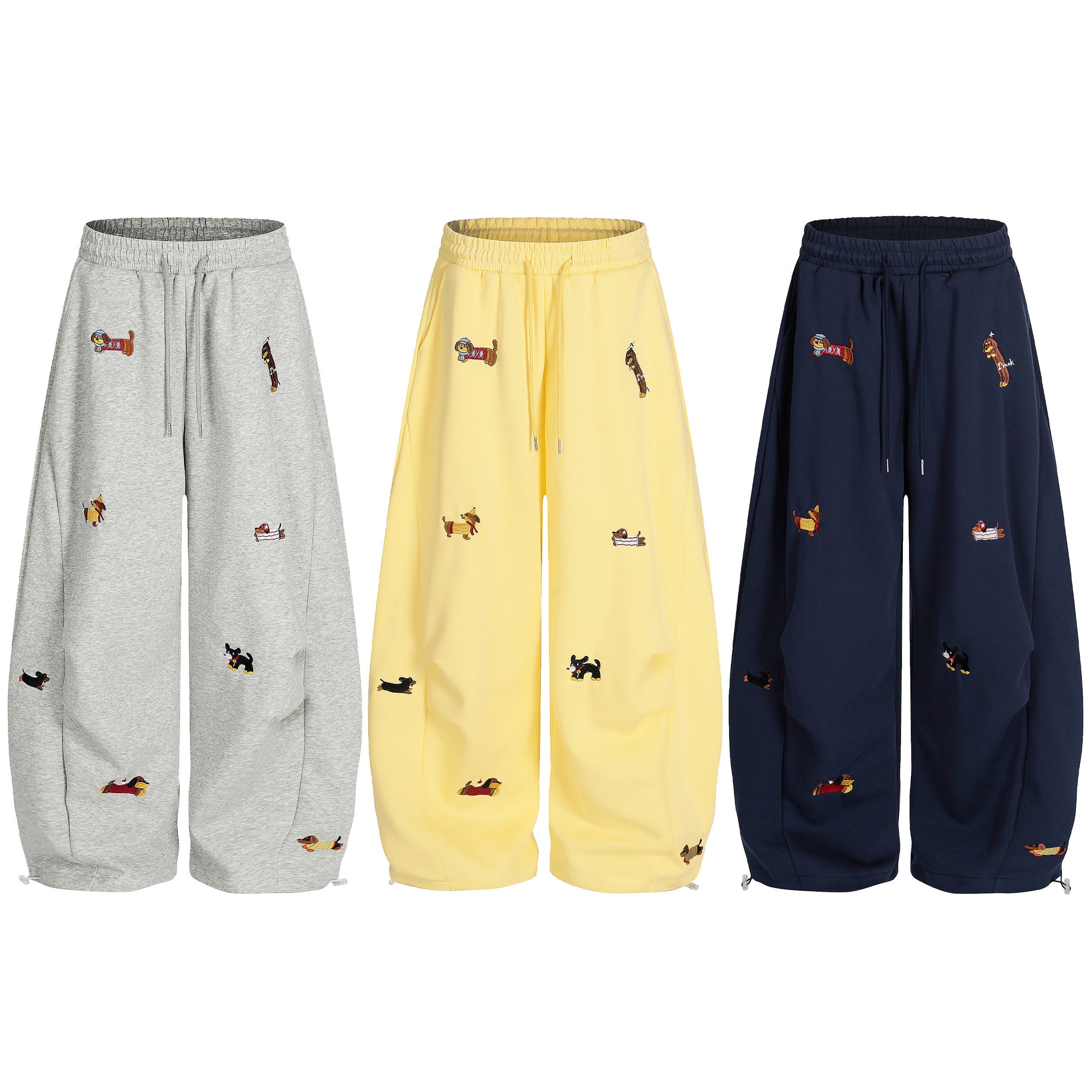 Three wide-leg sweatpants in grey, yellow, and navy with multicolor embroidered dog motifs, shown front view on white backgro