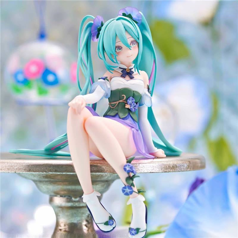 The Hatsune Miku Fairy 13.5cm PVC figure features long turquoise hair with twin tails and a white and purple outfit, sitting on a metallic platform. Its fairy-inspired design is enhanced by soft, blurry floral elements. Ideal for display.