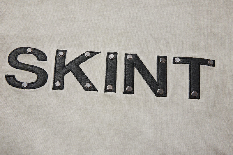 Vintage washed beige heavyweight tee with black SKINT lettering and metal rivet details