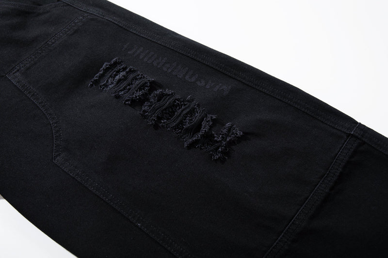 Close-up of black distressed denim leg with frayed tear details