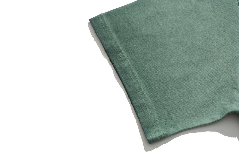 Close-up of a green vintage wash graphic tee sleeve with visible seam stitching and soft faded cotton texture