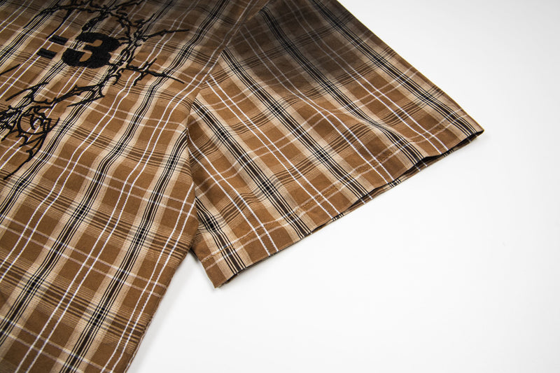 Brown plaid short-sleeve shirt with black graphic print and vintage streetwear style on a white background