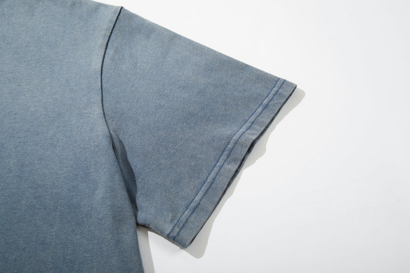 Close-up of a light blue vintage-washed graphic T-shirt sleeve with stitched cuff on a white background