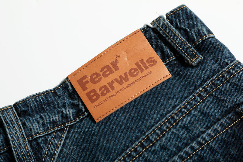 Close-up of tan leather-look logo patch on the back waistband of dark wash jeans