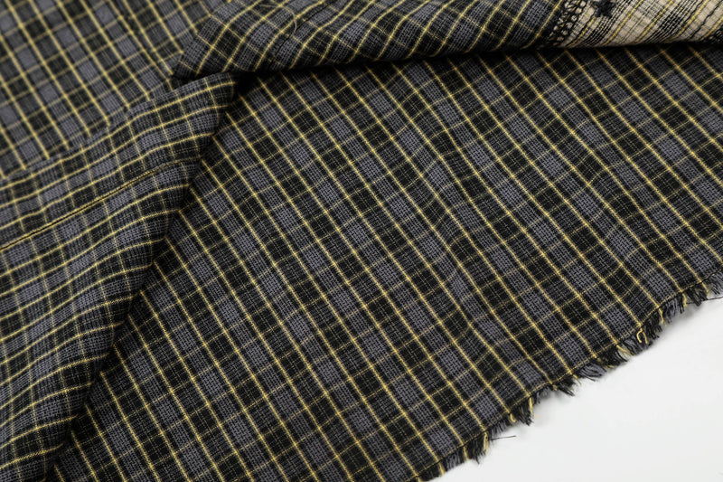 Close-up of black and gray plaid shirt fabric with yellow grid lines and raw frayed hem detail