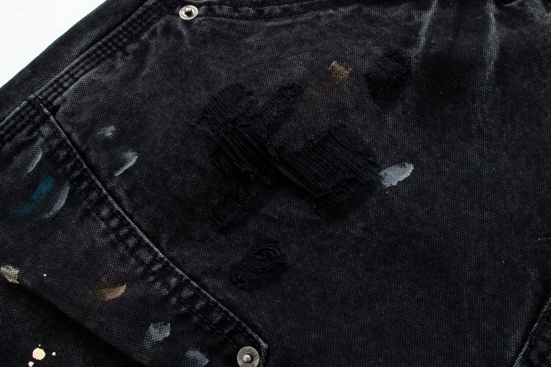 Close-up of black denim with distressed paint marks and frayed ripped patch