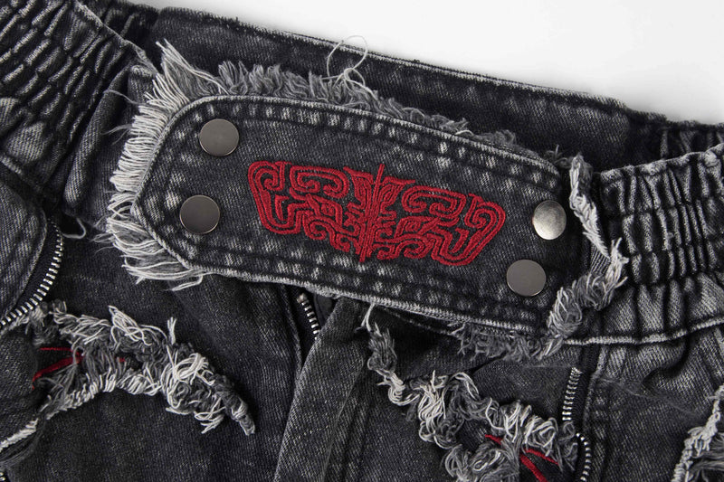 Close-up of back waistband patch with red embroidery, frayed denim edges, and metal rivets