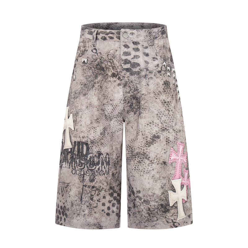Front view of washed gray denim shorts with black grunge print and pink cross patch